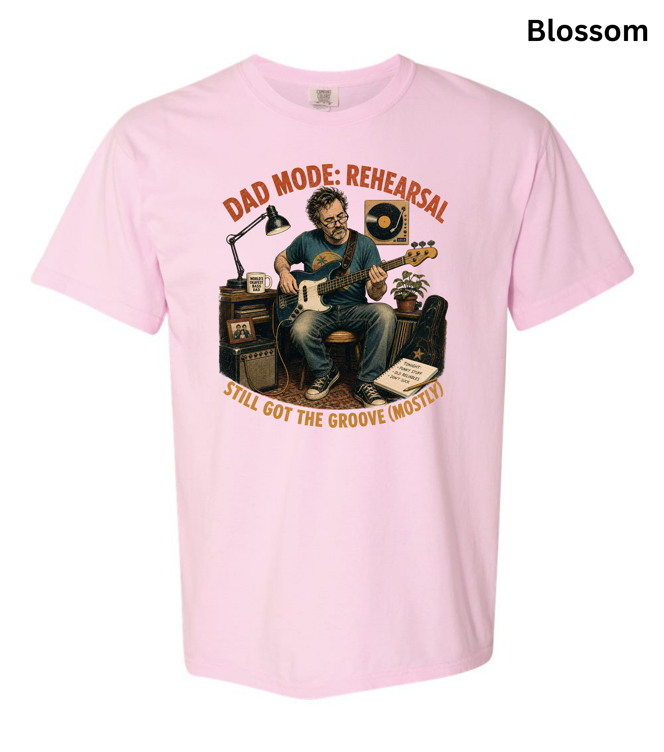 A light pink short-sleeve t-shirt with a graphic print of a man playing guitar in a rehearsal room, with the text 'DAD MODE: REHEARSAL' and 'STILL GOT THE GROOVE (MOSTLY!)' in orange. The word 'Blossom' is printed in black in the top right corner.