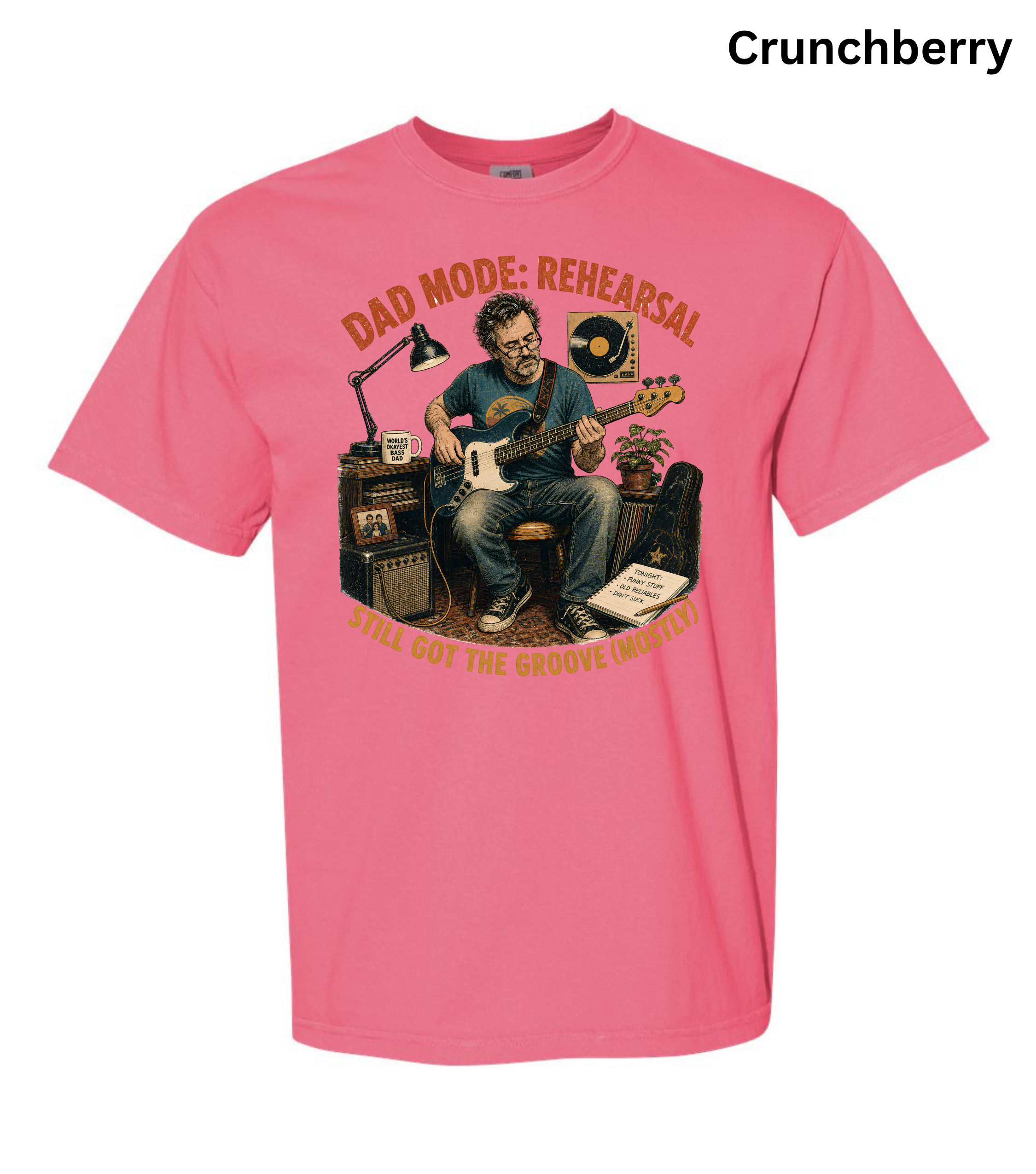 A pink short-sleeve crewneck t-shirt featuring a graphic illustration of a man playing an electric guitar in a rehearsal room, with the text 'DAD MODE: REHEARSAL' and 'I'M GOTTIN' THE REHEARSAL VIDEO!' in orange. The word 'Crunchberry' is printed in black in the top right corner.