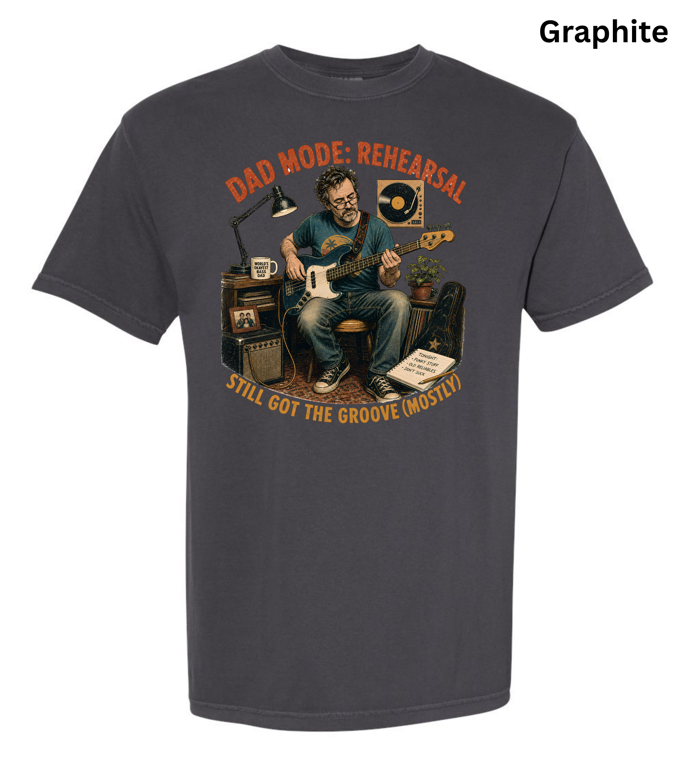 A dark charcoal gray t-shirt with a vintage-style graphic of a man playing an electric guitar in front of audio equipment. The graphic features orange text reading 'DAD MODE: REHEARSAL' and 'STILL GOT THE GROOVE (MOST!)'.
