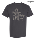 A dark charcoal gray t-shirt with a white line art graphic of a man playing an acoustic guitar on a stool, next to the quote 'Music heals what words cannot.' The word 'Graphite' is printed in black in the top right corner, indicating the fabric color.