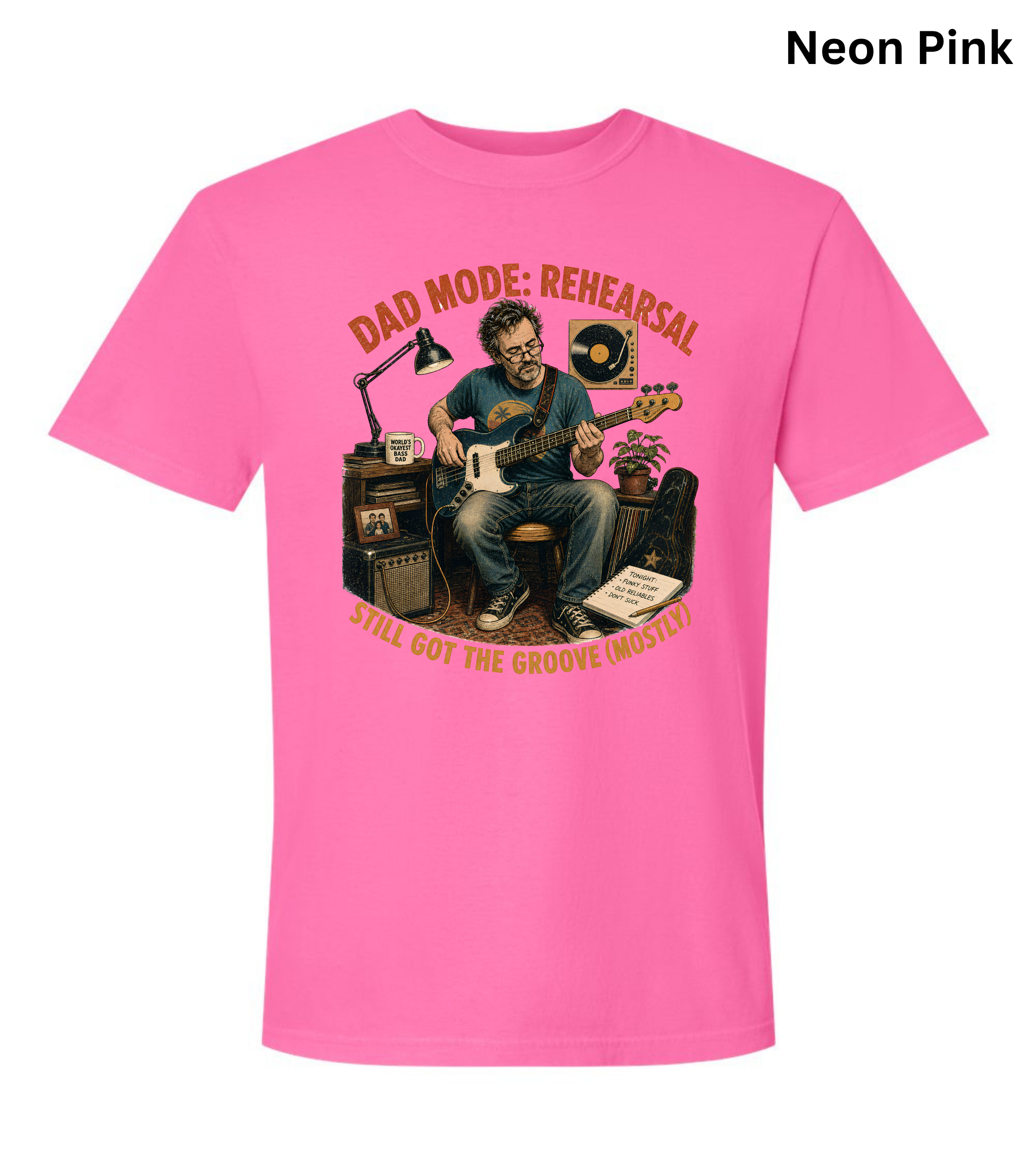 A bright neon pink short-sleeve t-shirt with a vintage-style graphic of a man playing an electric guitar in a rehearsal studio. The graphic features the text 'DAD MODE: REHEARSAL' at the top and 'YEAH GOT THE GROOVE INSTINCT!' at the bottom in a warm yellow-orange tone.