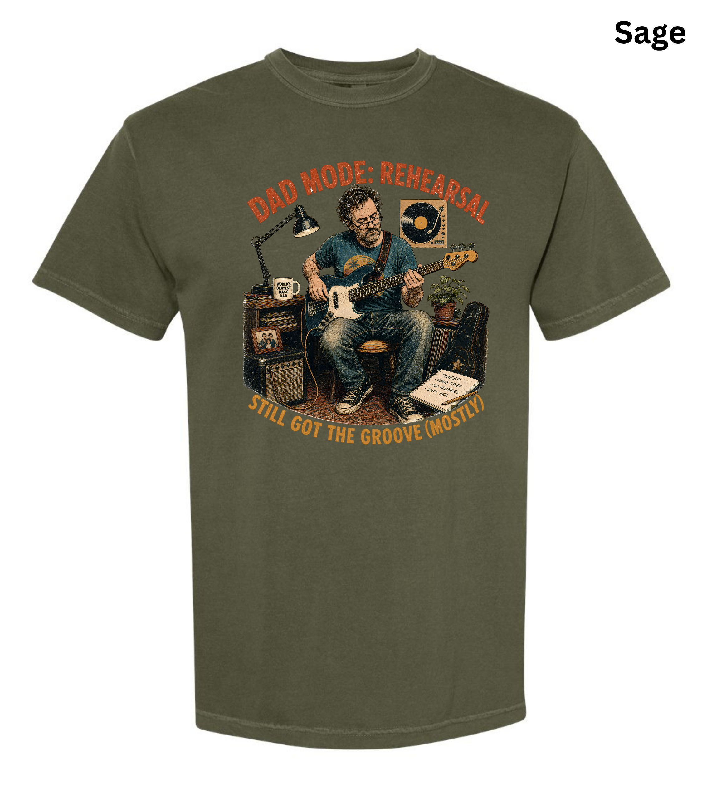 An olive sage green short-sleeve t-shirt with a vintage-style graphic of a man playing an electric guitar in a rehearsal room. The graphic features orange text reading 'DAD MODE: REHEARSAL' and 'STILL GOT THE GROOVE (MOSTLY?)'.