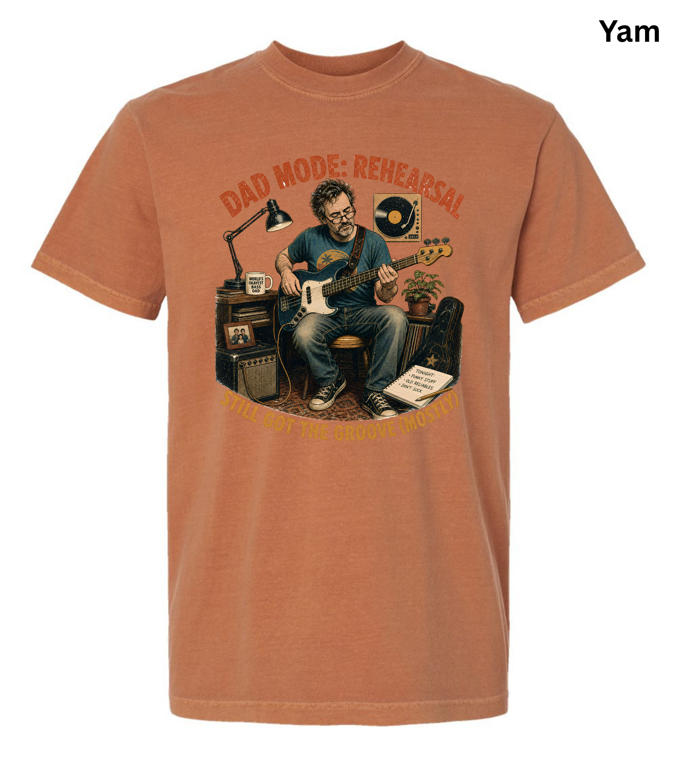 A short-sleeve crewneck t-shirt in a warm rust or terracotta color, featuring a large graphic print of a man in a rehearsal room with the text 'DAD MODE: REHEARSAL'. The shirt is displayed flat against a white background, with a small 'Yam' label in the top right corner.