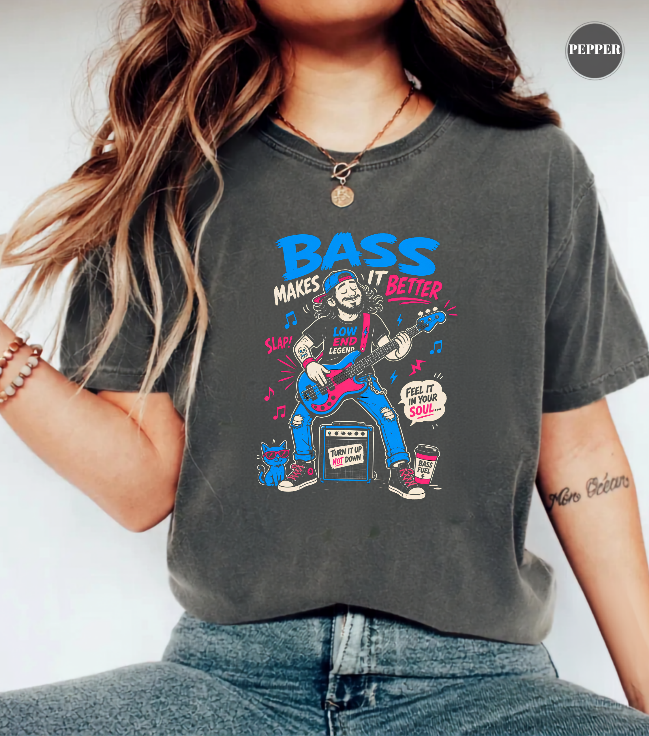 A woman wearing a dark gray graphic t-shirt with a colorful 'Bass Makes It Better' illustration, paired with blue jeans. The image is a close-up lifestyle shot showing the fit of the shirt.