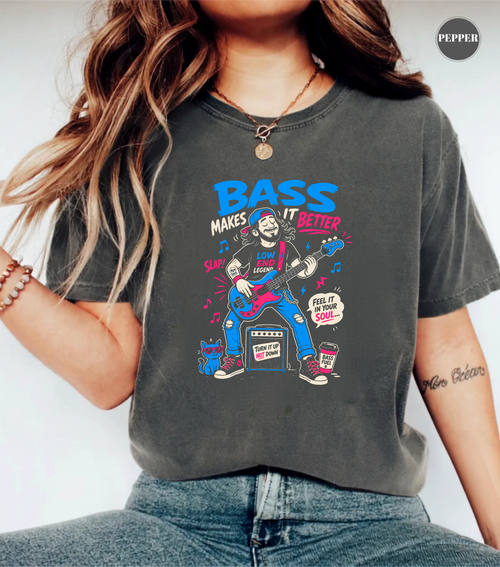 A woman wearing a dark gray graphic t-shirt with a colorful 'Bass Makes It Better' illustration, paired with blue jeans. The image is a close-up lifestyle shot showing the fit of the shirt.