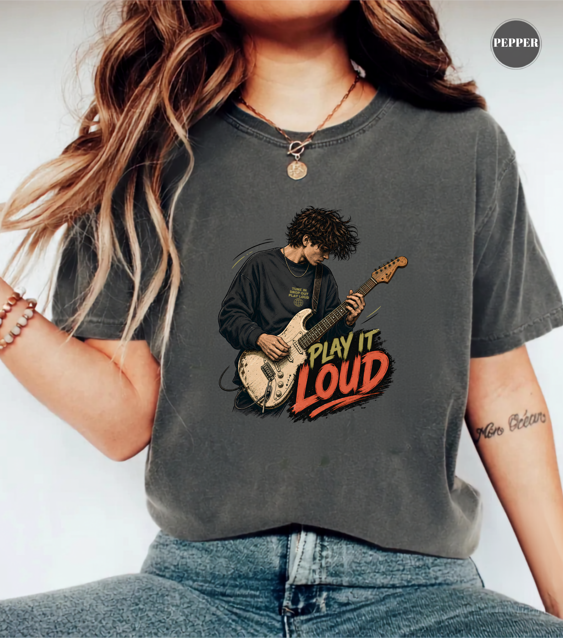 A woman wearing a dark gray graphic t-shirt with a vintage-style illustration of a guitarist playing and the text 'PLAY IT LOUD'.