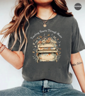 A woman wearing a dark gray graphic t-shirt with a vintage piano and floral design that reads 'Teaching Hearts Through Music'.