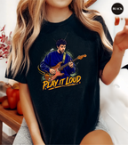 A woman wearing a black graphic t-shirt featuring an illustration of a man playing an electric guitar with the text 'PLAY IT LOUD' in yellow. The image is a lifestyle shot with a 'BLACK' color badge in the top right corner.
