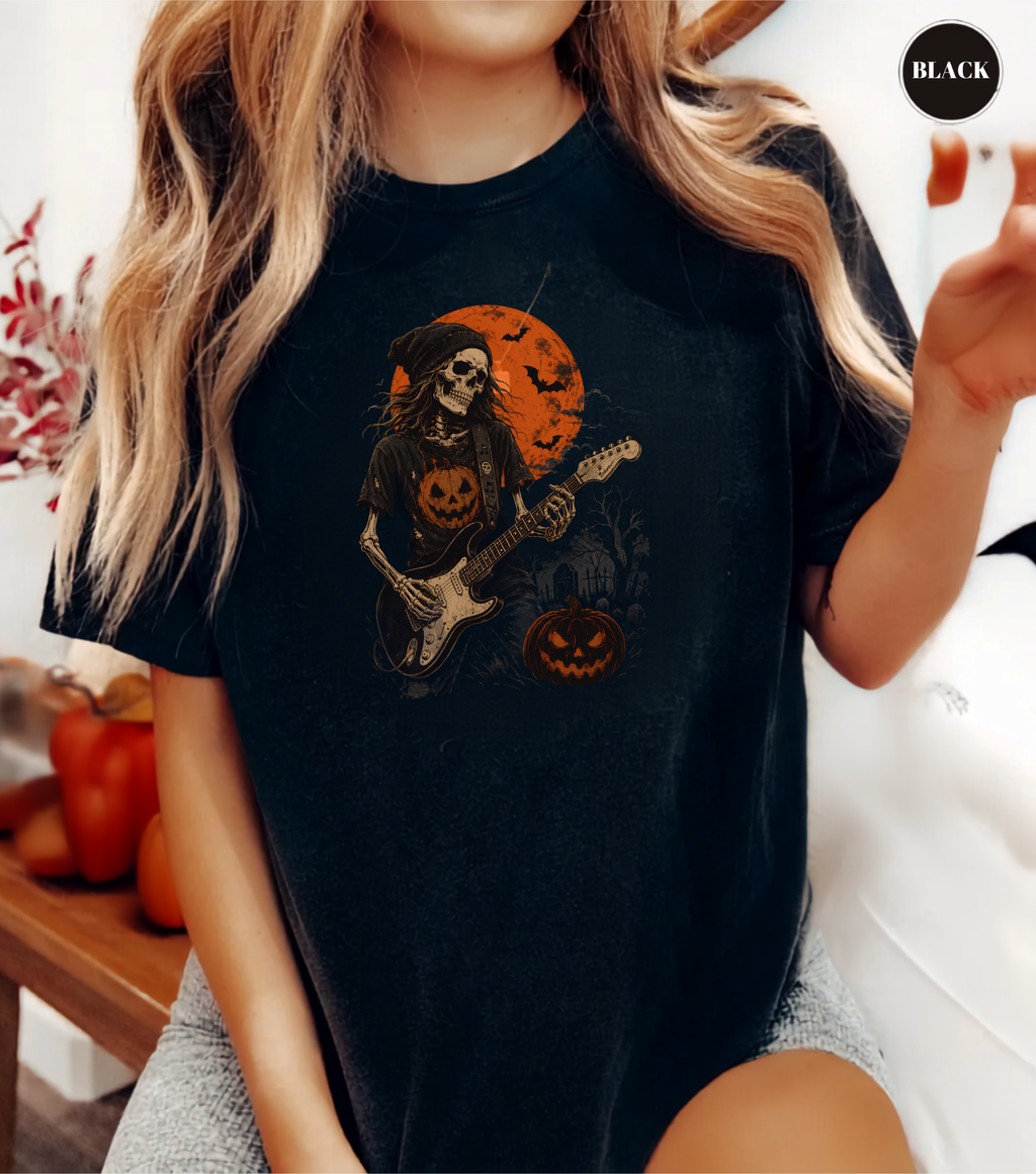 A woman wearing a black graphic t-shirt featuring a skeleton playing an electric guitar in front of an orange full moon and jack-o'-lanterns. The image has a 'BLACK' label in the top right corner.