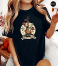 A woman wearing a black graphic t-shirt with a vintage-style guitar, roses, and musical notes design that reads 'Melody & Thorns'.