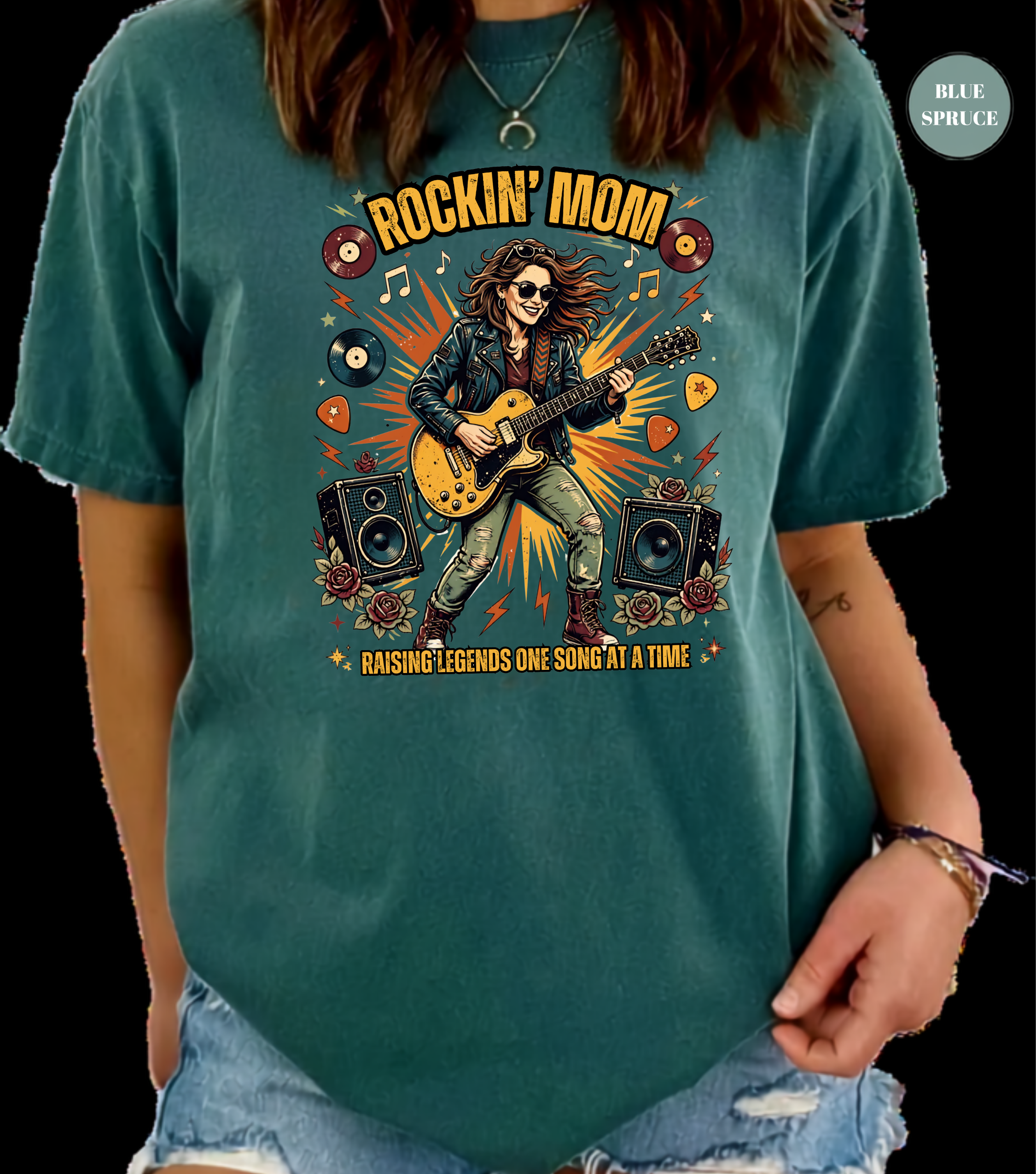 A woman wearing a teal graphic t-shirt with a 'Rockin' Mom' guitar player design, paired with distressed denim shorts, shown against a black background.