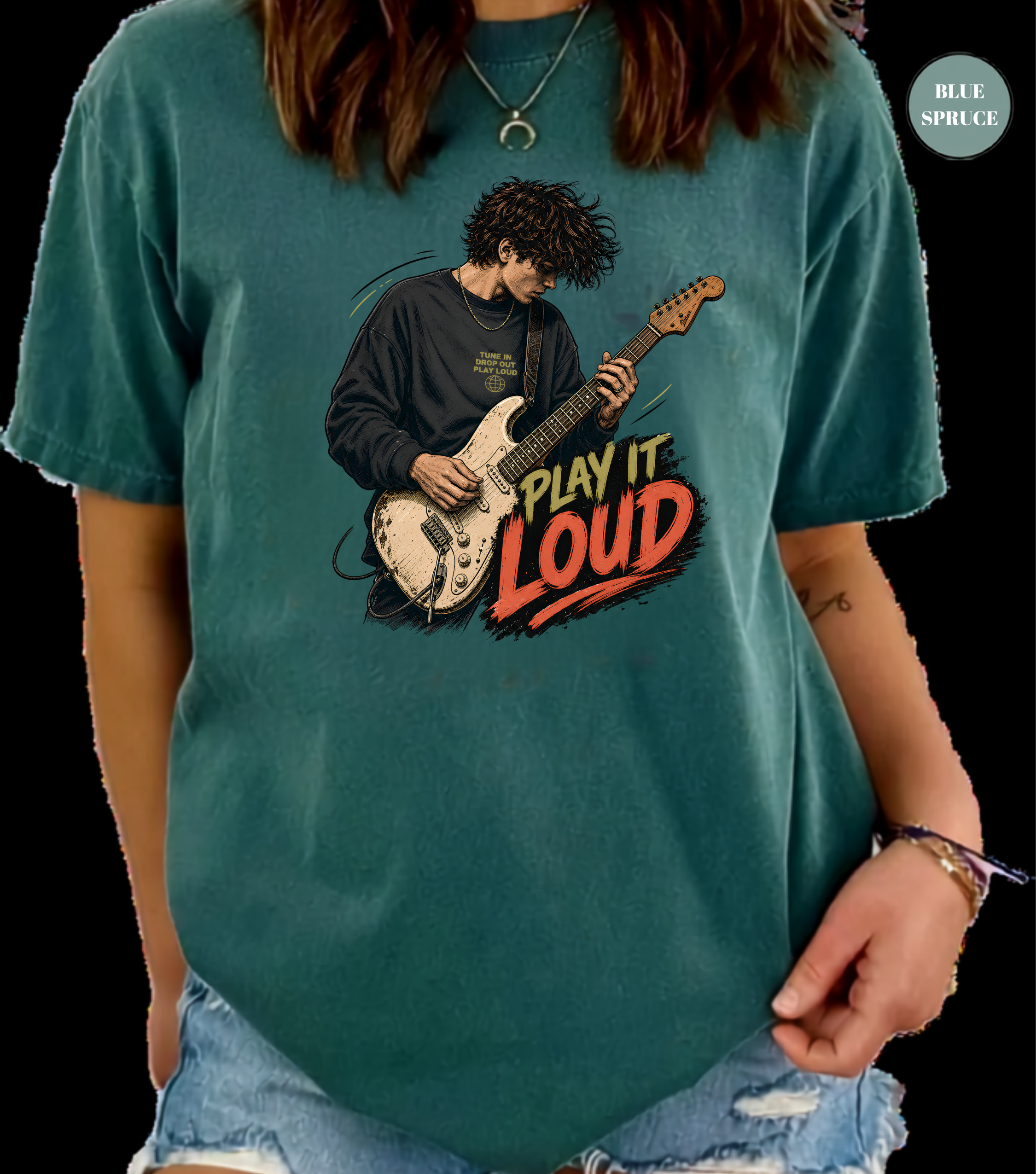 A person wearing a teal graphic t-shirt with a vintage-style illustration of a guitarist and the text 'PLAY IT LOUD'. The image has a black background and a 'BLUE SPRUCE' brand badge in the top right corner.