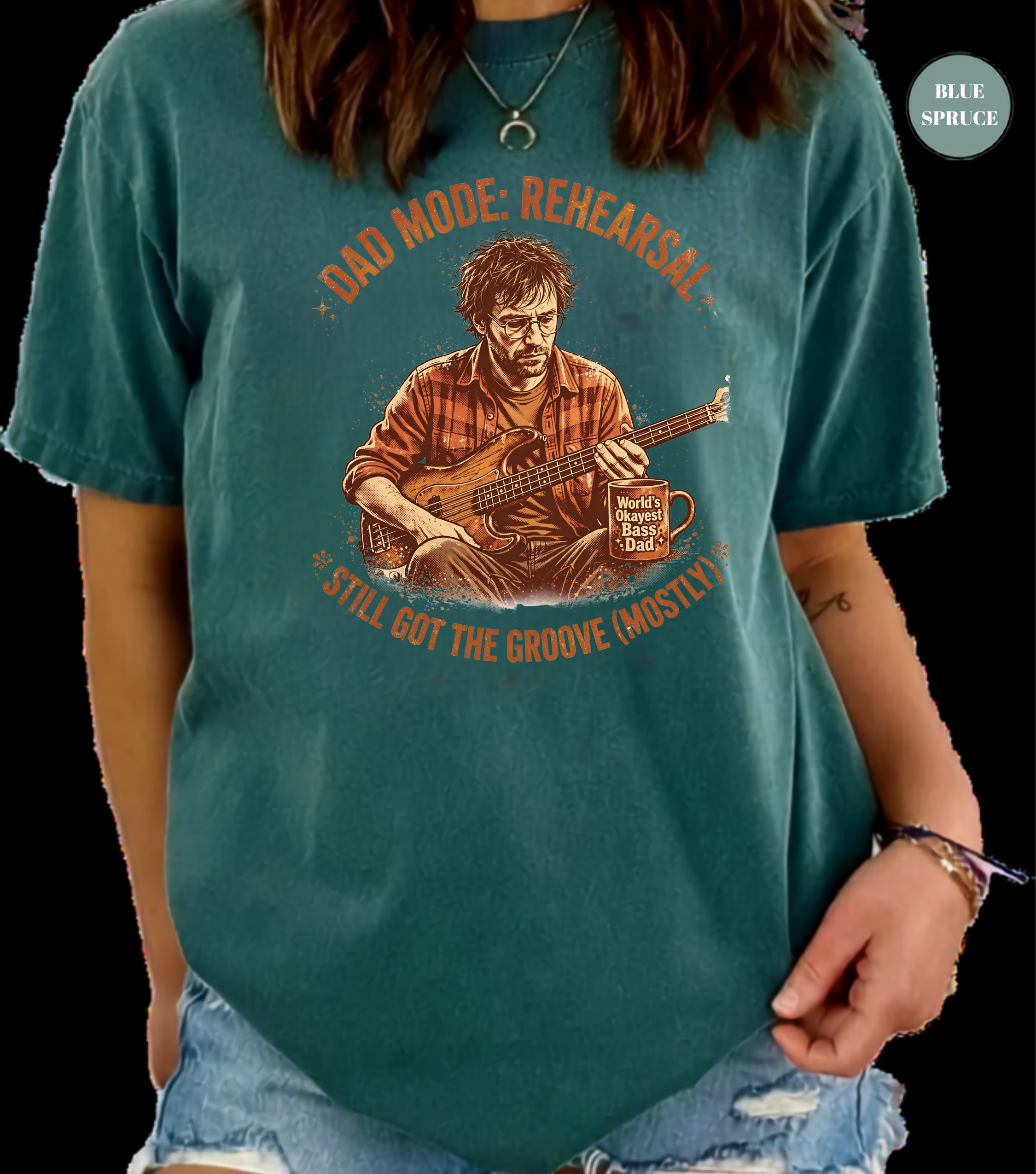 A person wearing a teal graphic t-shirt with a vintage-style print of a man playing a guitar and the text 'DAD MODE: REHEARSAL.
