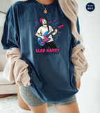 A woman wearing an oversized navy blue graphic t-shirt with a colorful illustration of a guitarist and the text 'SLAP HAPPY'. She has beige ribbed knit sleeves draped off her shoulders and is wearing gray shorts.