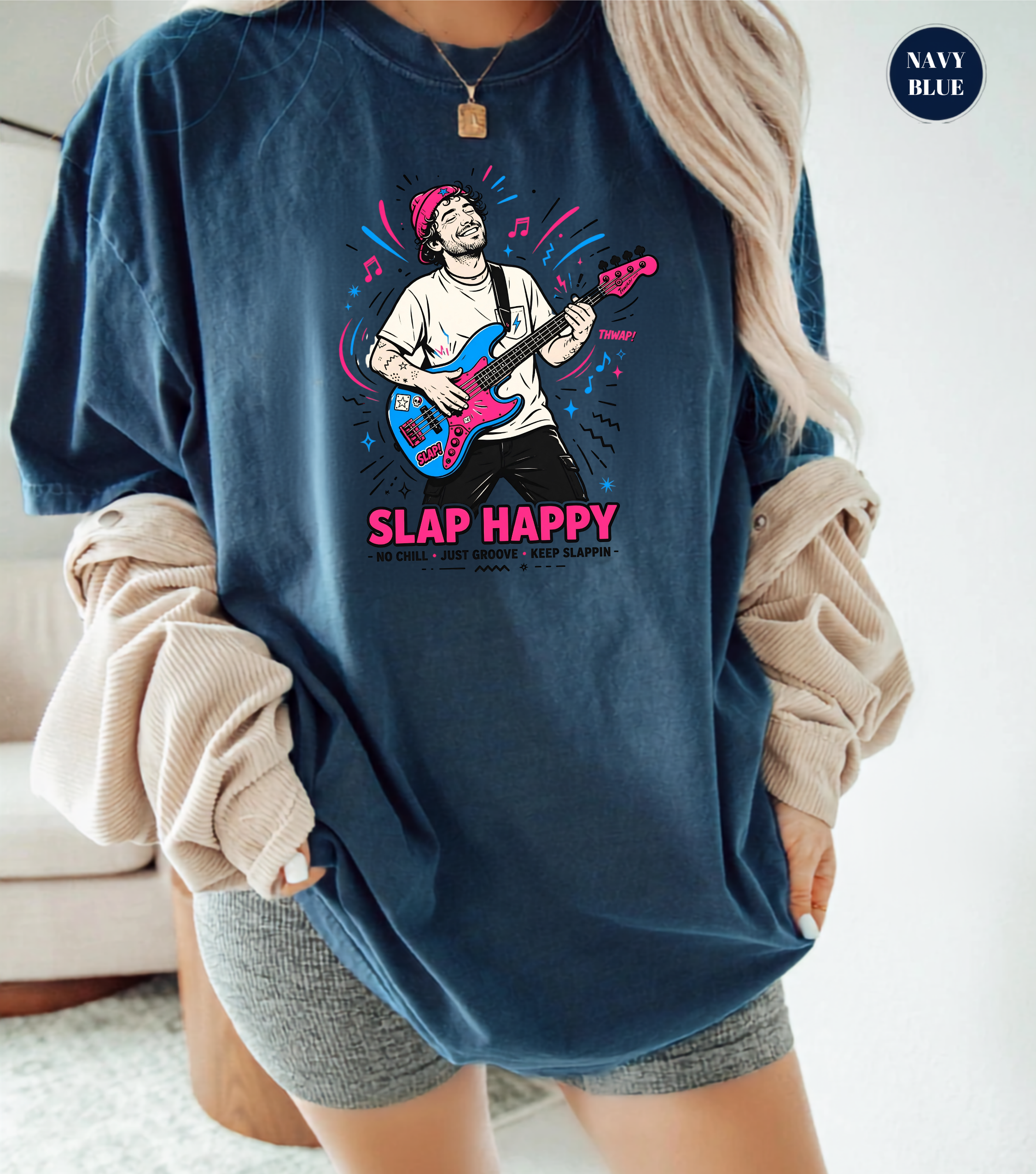 A woman wearing an oversized navy blue graphic t-shirt with a colorful illustration of a guitarist and the text 'SLAP HAPPY'. She has beige ribbed knit sleeves draped off her shoulders and is wearing gray shorts.