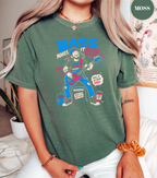A woman wearing a green graphic t-shirt with a colorful illustration of a girl playing a guitar and the text 'BASS MAKES IT BETTER'. The brand name 'MOSS' is visible in a green circle in the top right corner.