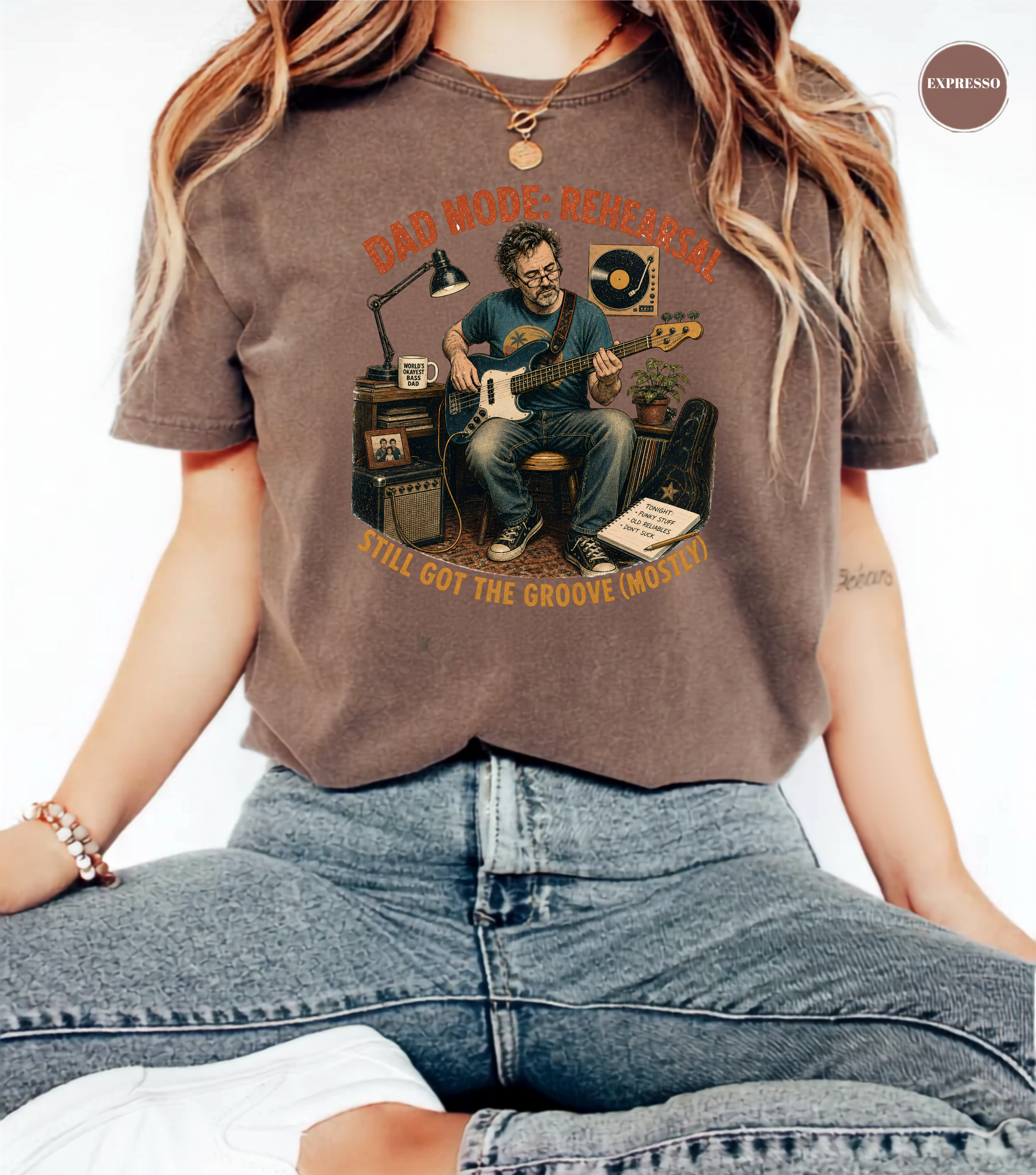 A person wearing a faded brown graphic t-shirt with a vintage-style illustration of a man playing an electric guitar in a recording studio. The text on the shirt reads 'BAD MODE.
