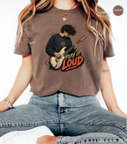 A woman wearing a brown cropped graphic t-shirt with a guitar player illustration and the text 'PLAY IT LOUD'.