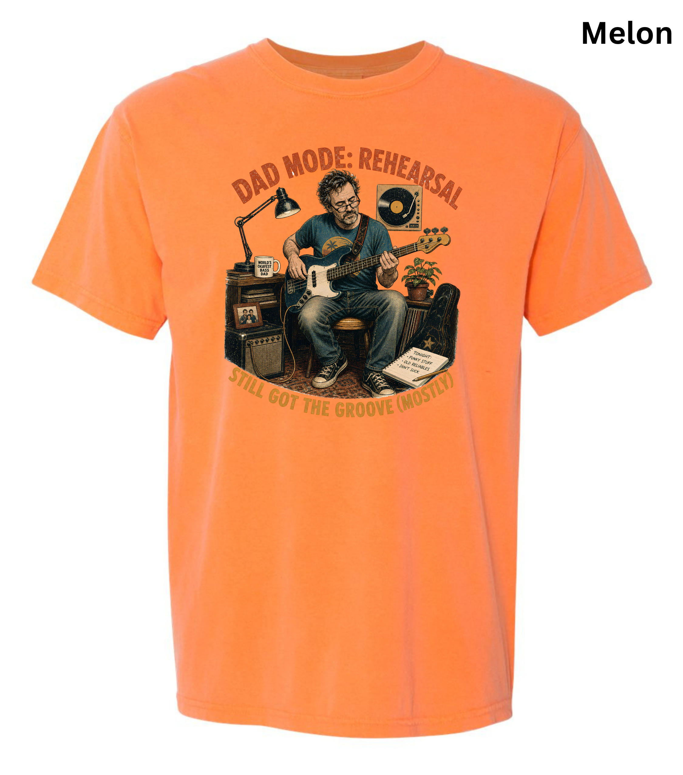 An orange short-sleeve t-shirt with a graphic print of a man playing guitar in front of amplifiers, with the text 'DAD MODE: REHEARSAL' and 'I STILL GOT THE GROOVE MUSHED!' printed around him. The word 'Melon' is written in the top right corner.