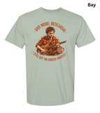 A light sage green graphic t-shirt on a white background, featuring a vintage-style illustration of a man playing guitar with the text 'DAD MODE: REHEARSAL' and 'STILL GOT THE GROOVE (MOSTLY)'. A small 'Bay' label is visible in the top right corner.