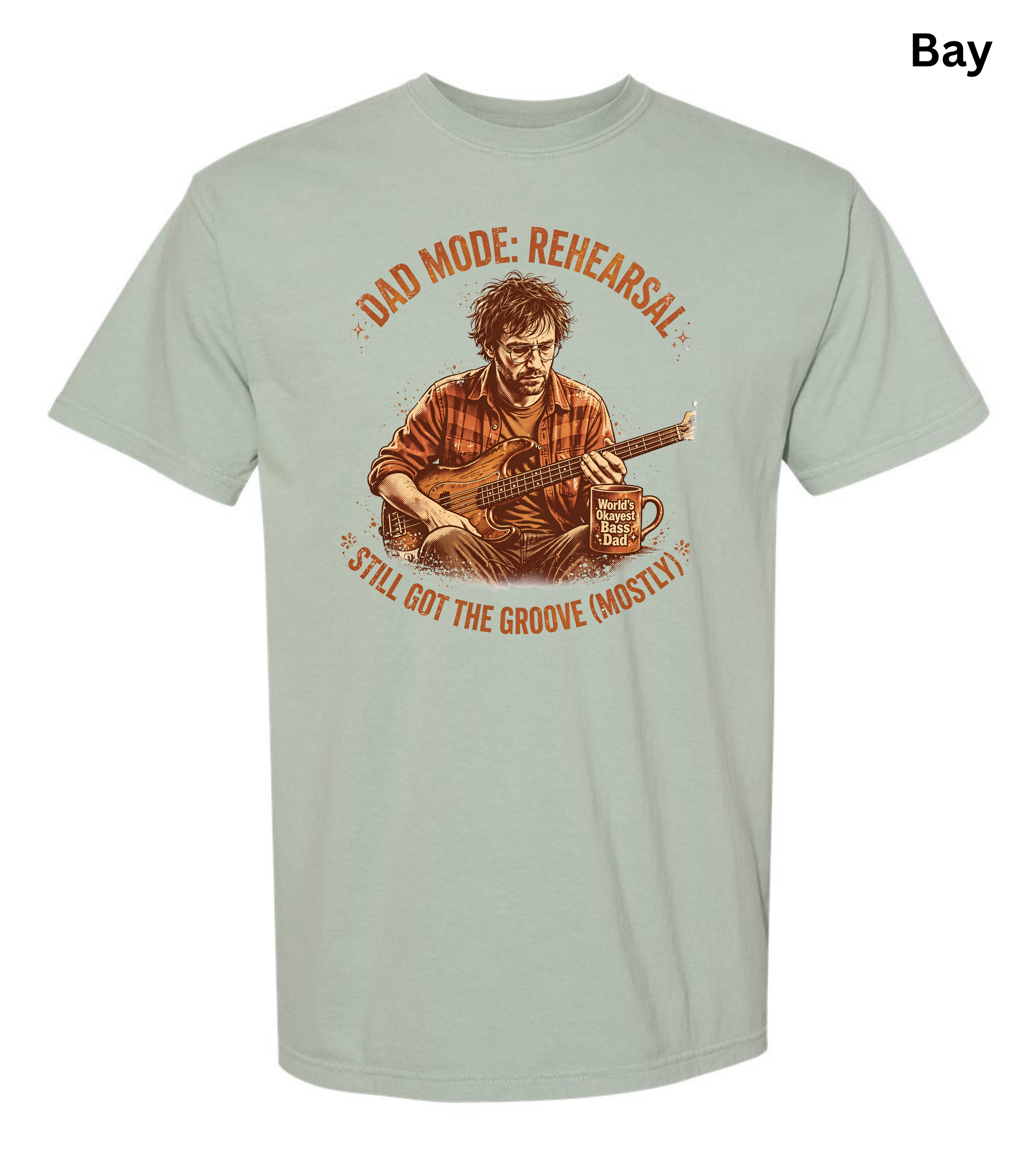 A light sage green graphic t-shirt on a white background, featuring a vintage-style illustration of a man playing guitar with the text 'DAD MODE: REHEARSAL' and 'STILL GOT THE GROOVE (MOSTLY)'. A small 'Bay' label is visible in the top right corner.